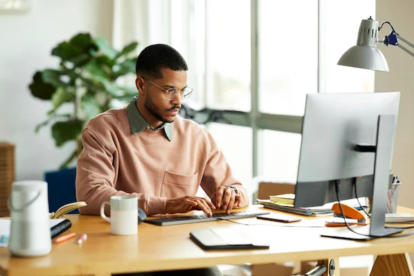 man sitting at desk by computer writing on a pad; i am a marketer